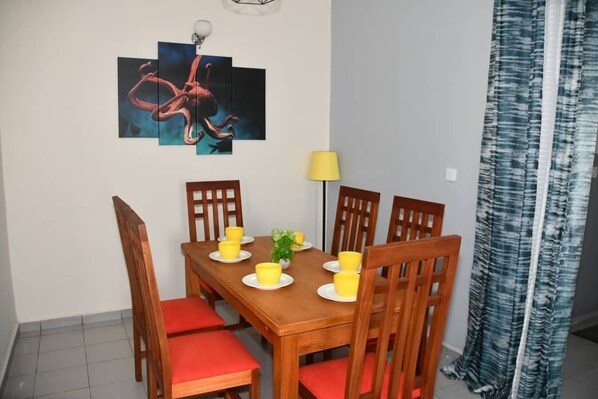 Un coin repas avec une table en bois dressée pour quatre personnes, des chaises rembourrées de couleur rouge et un tableau accroché au mur.