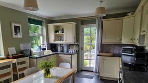 A compact kitchen with a dining area, featuring a sink, stove, and cabinets. - Cosy Cottage overlooking the Teifi Gorge (Cilgerran)