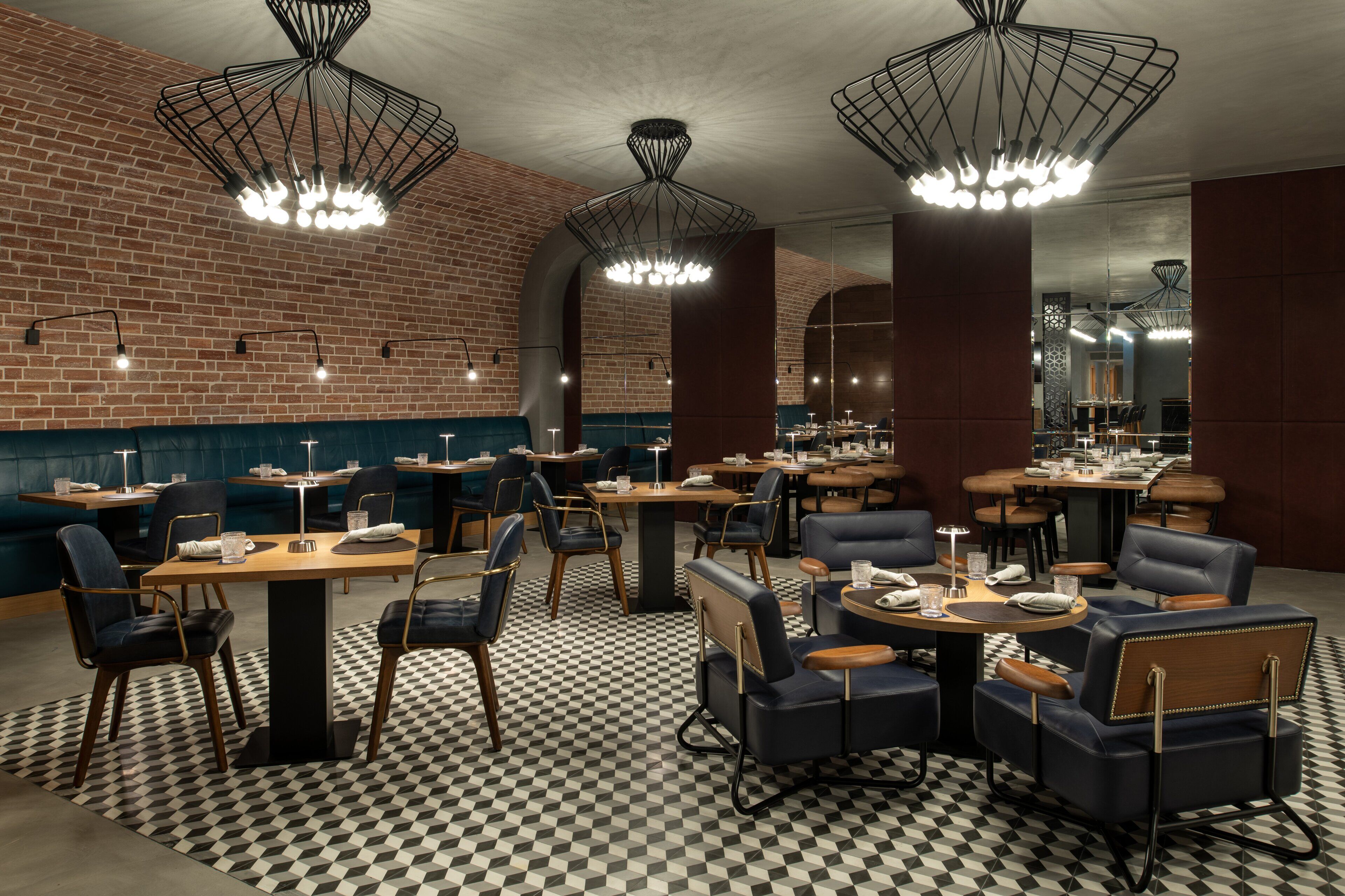 Ein Restaurant mit Schachbrettboden, dunkelblauen Polsterstühlen und moderner Pendelleuchten.