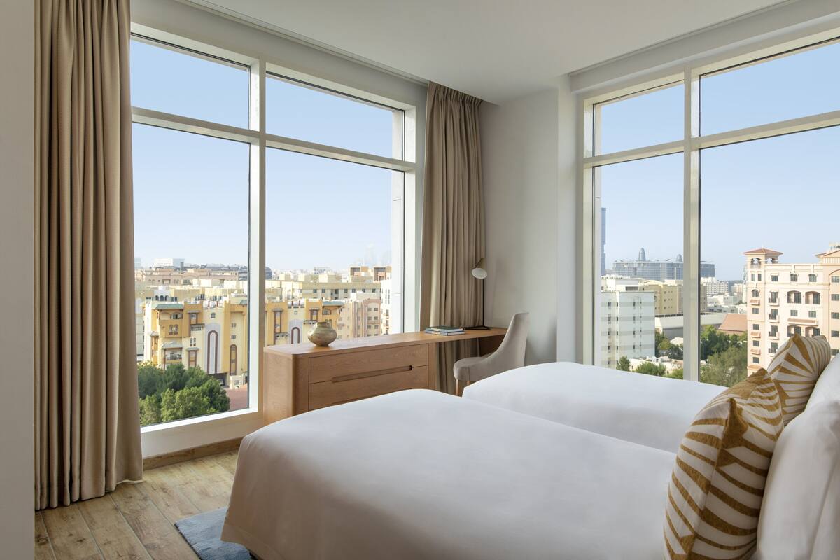 Habitación de hotel con ventanas amplias, un escritorio y dos camas.