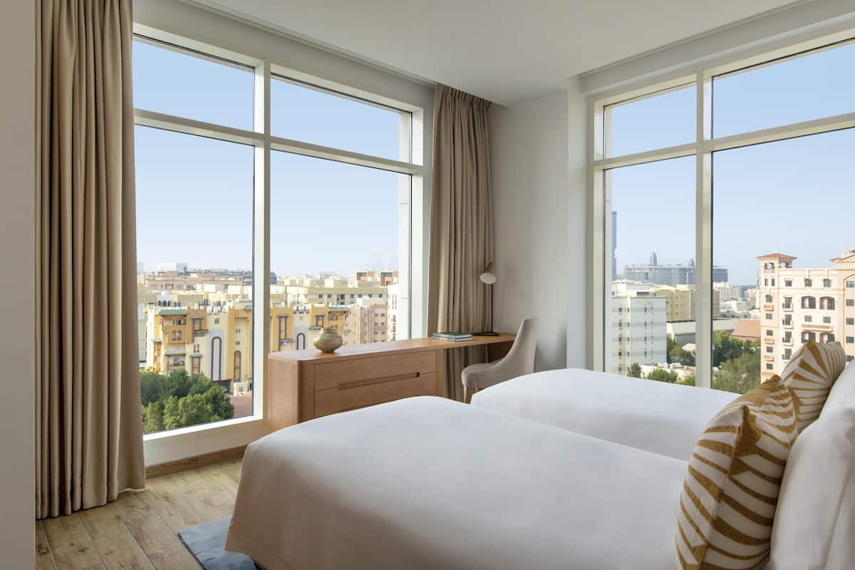 Une chambre d’hôtel avec de grandes fenêtres, un bureau et deux lits.