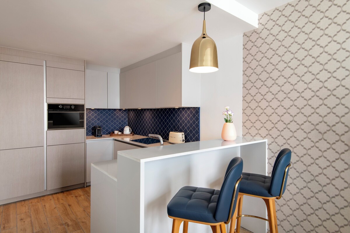 A modern kitchen with a central island, bar stools, and a pendant light.