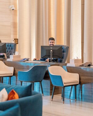 A modern hotel lobby with a central reception desk, comfortable seating, and a large window with curtains. - Abesq Doha Hotel and Residences - An IHG Hotel (Doha)