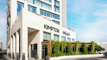 A modern building with the name 'KIMPTON' on the facade, featuring large windows and a covered outdoor area with greenery.