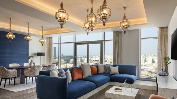 Una sala moderna con un sofá seccional azul, una mesita de centro de mármol y vistas a la ciudad a través de amplios ventanales.