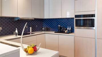 Una cocina moderna con armarios blancos, salpicadero azul, horno de acero inoxidable y una cesta de frutas sobre la encimera.