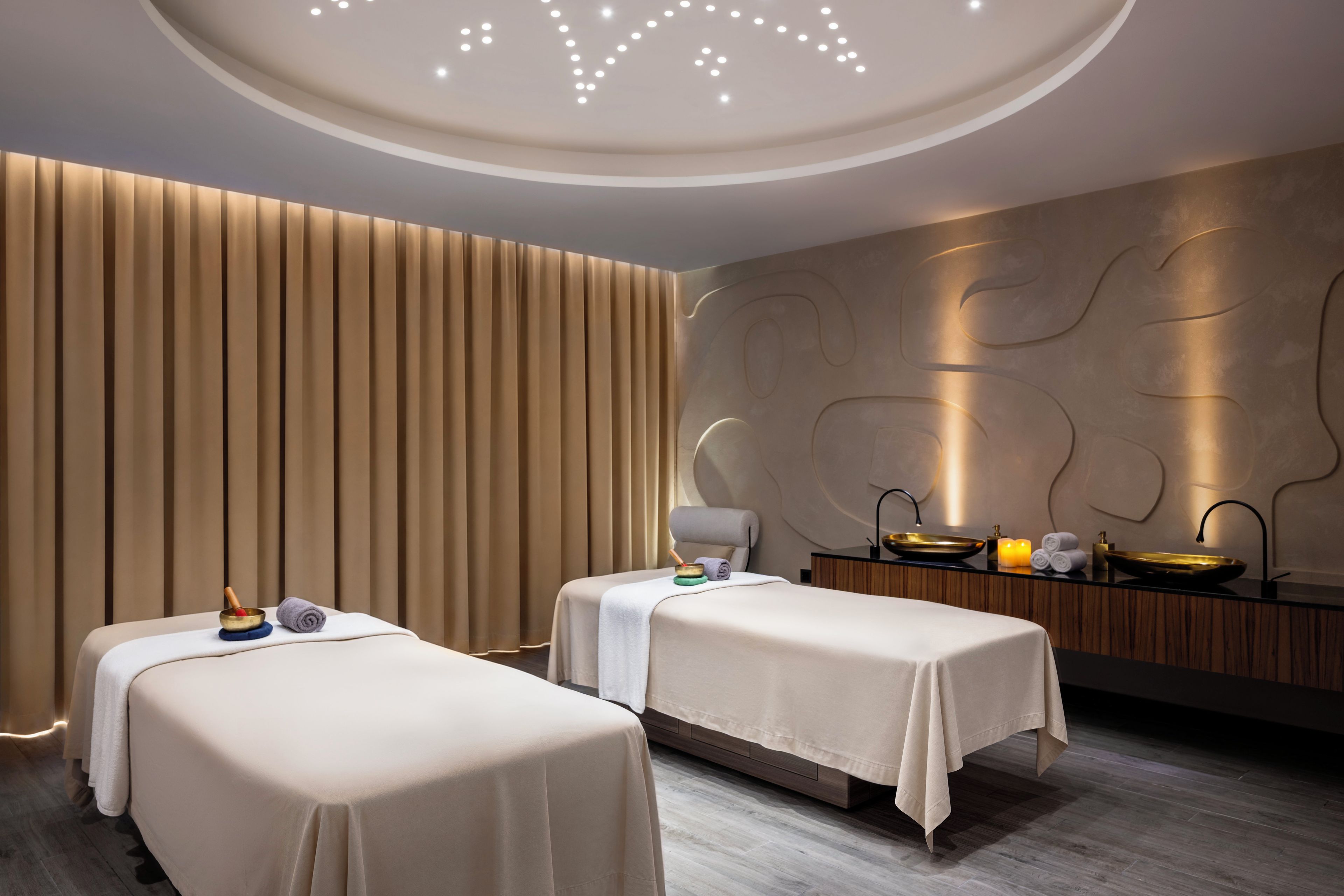 Un cuarto de spa con dos camillas de masaje, una pared de madera con listones verticales, un techo curvo con iluminación empotrada y un piso de madera.