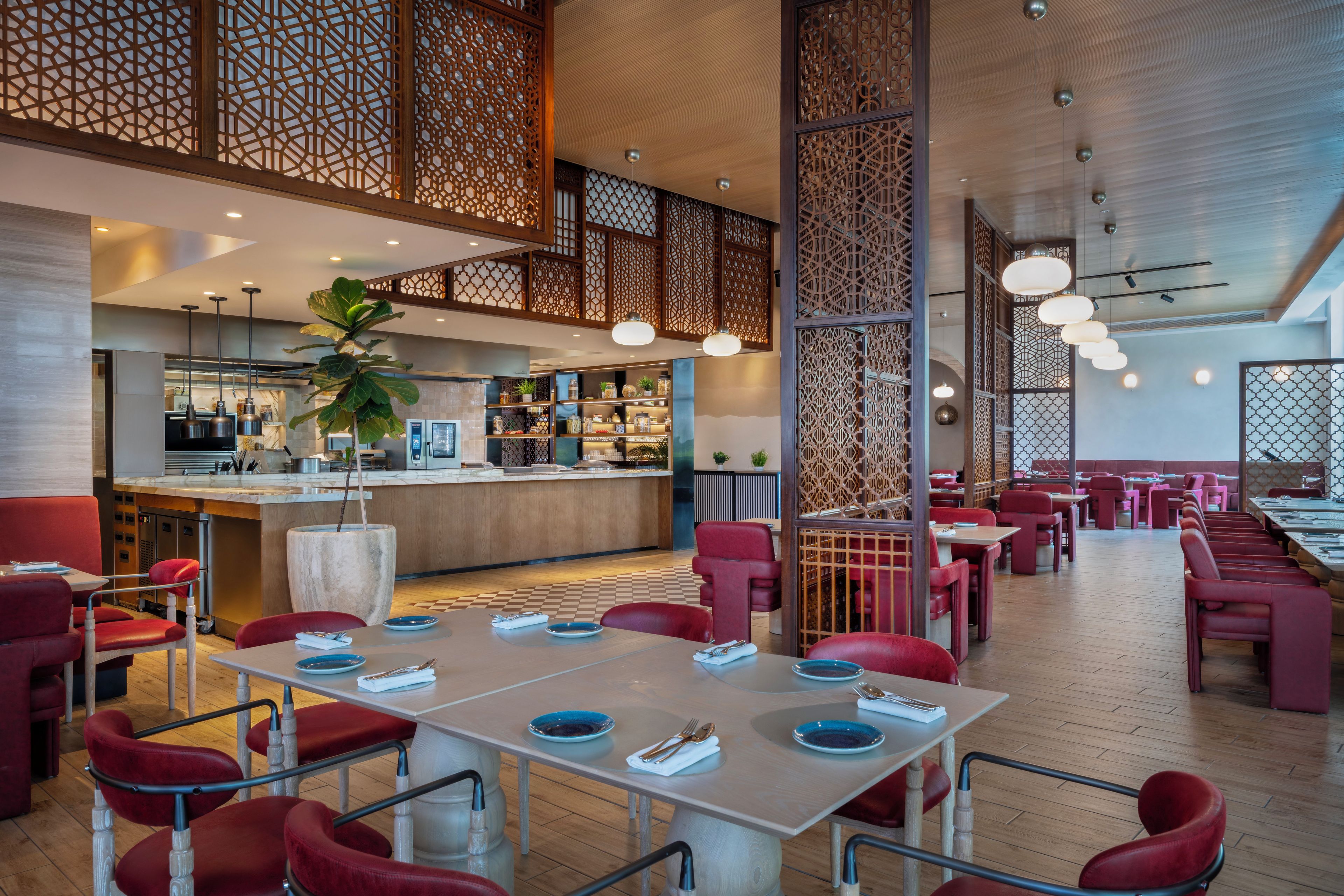A restaurant with a high ceiling, wooden paneling, and red upholstered chairs. Tables are set with blue plates and silverware.