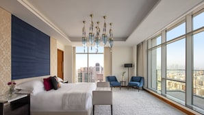 Amplia habitación de hotel con una cama grande, una zona de estar y vistas a la ciudad a través de amplios ventanales.