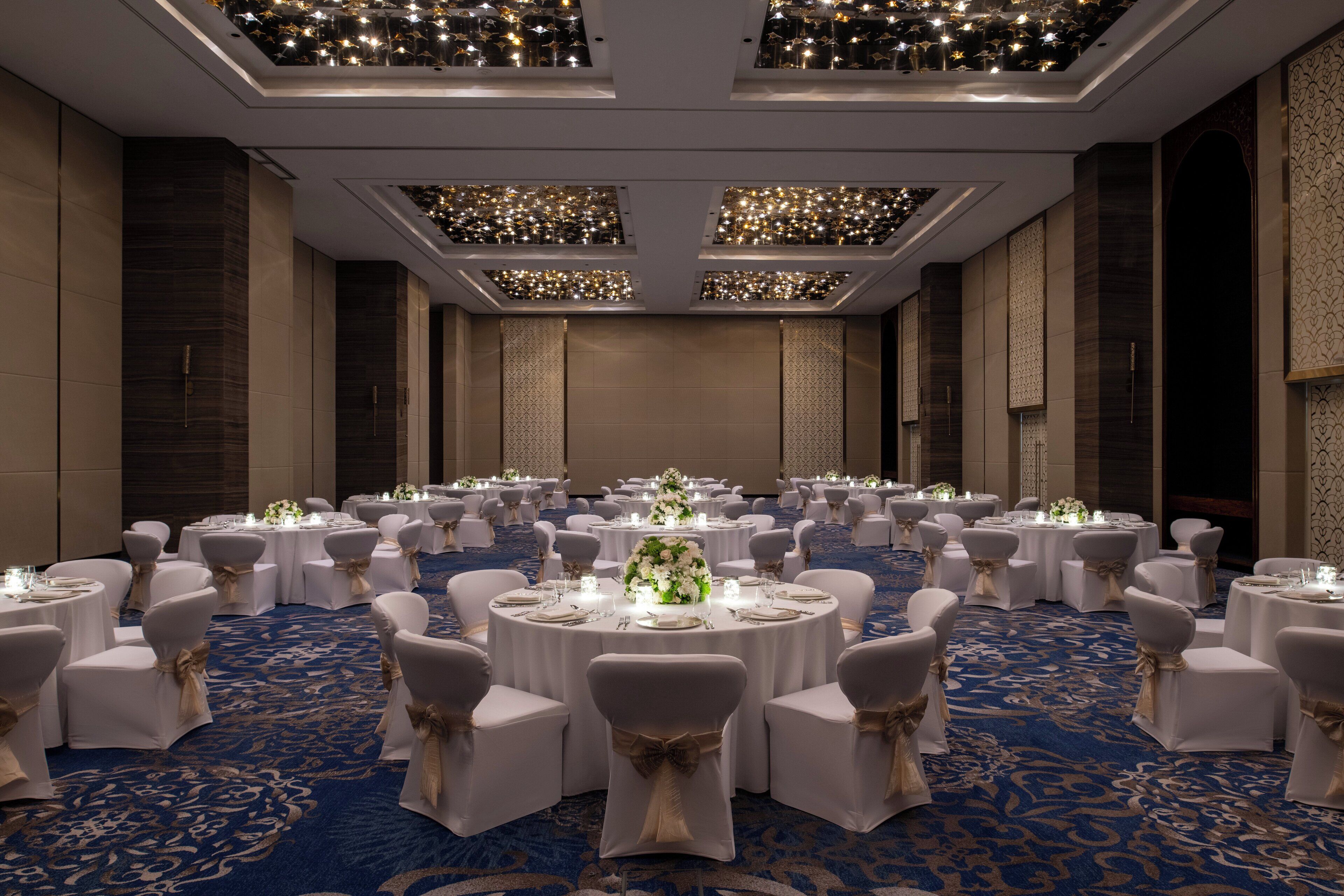 A banquet hall with round tables, white chairs, and floral centerpieces.