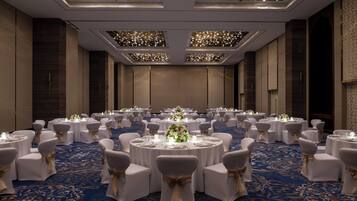 A banquet hall with round tables, white chairs, and floral centerpieces.