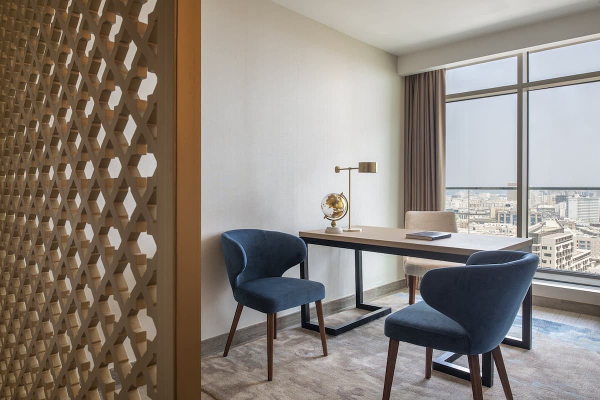 Una habitación de hotel moderna con vistas a la ciudad, un escritorio con dos sillas, un globo terráqueo sobre la mesa y un separador decorativo.