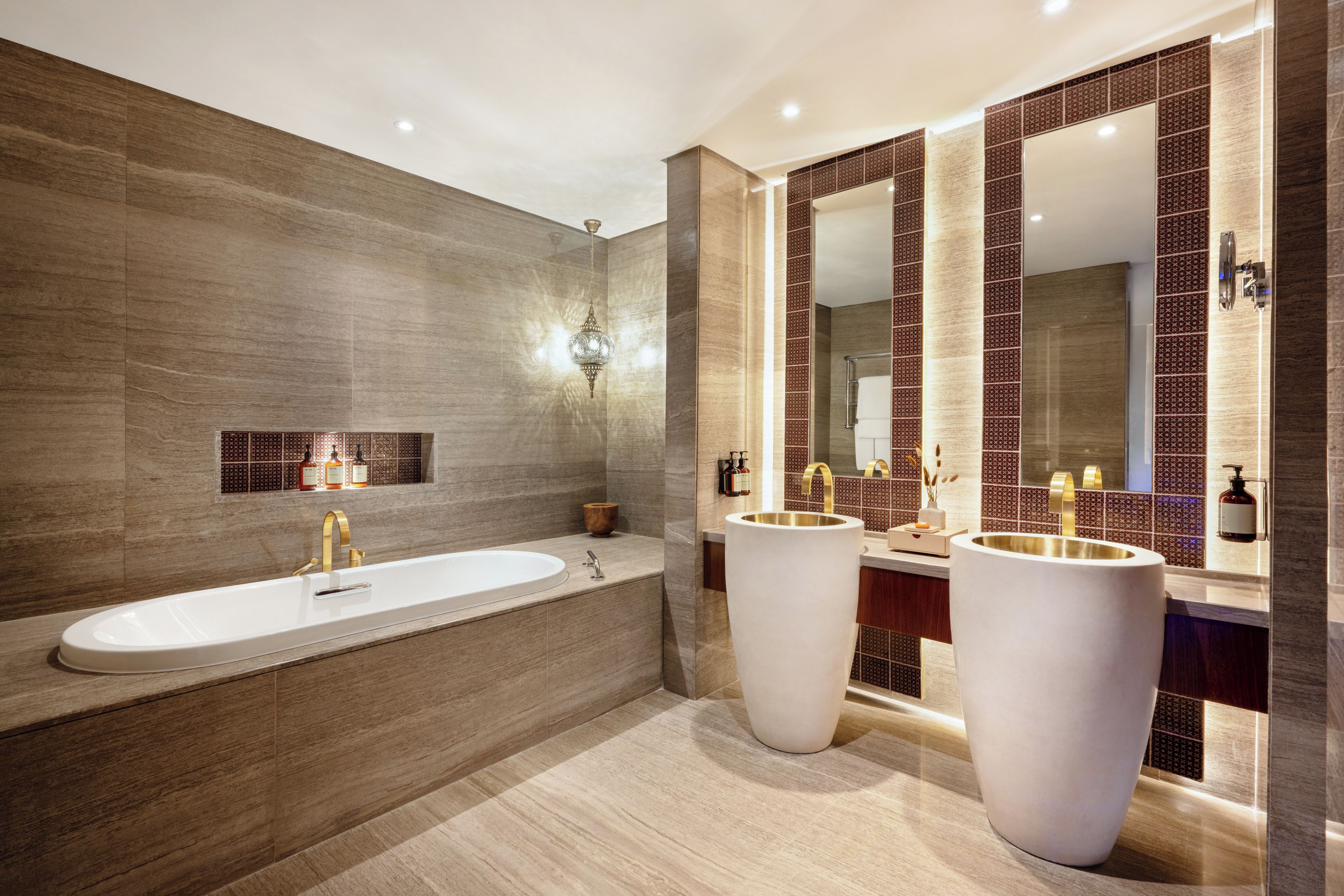 A modern bathroom with a large freestanding bathtub, two sinks with gold faucets, and a large mirror above the sinks.
