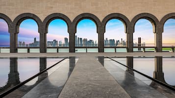 A waterfront promenade with a reflective pool and a city skyline view through arched openings.