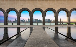 Un paseo marítimo con un estanque reflectante y vistas del horizonte urbano a través de arcos.