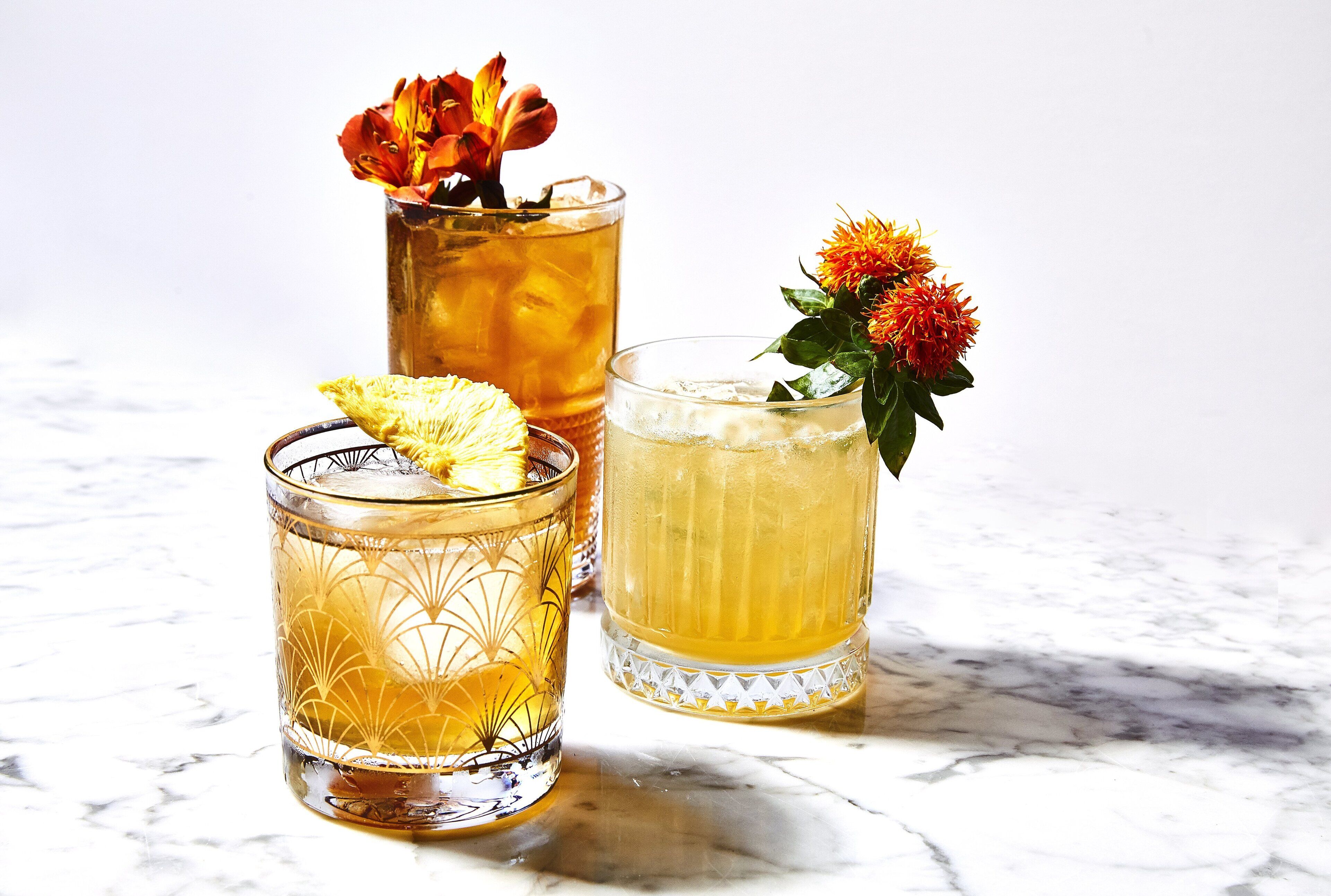 Three glasses of beverages with garnishes on a marble surface.