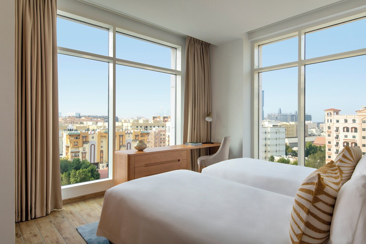 A hotel room with large windows, a desk, and two beds.