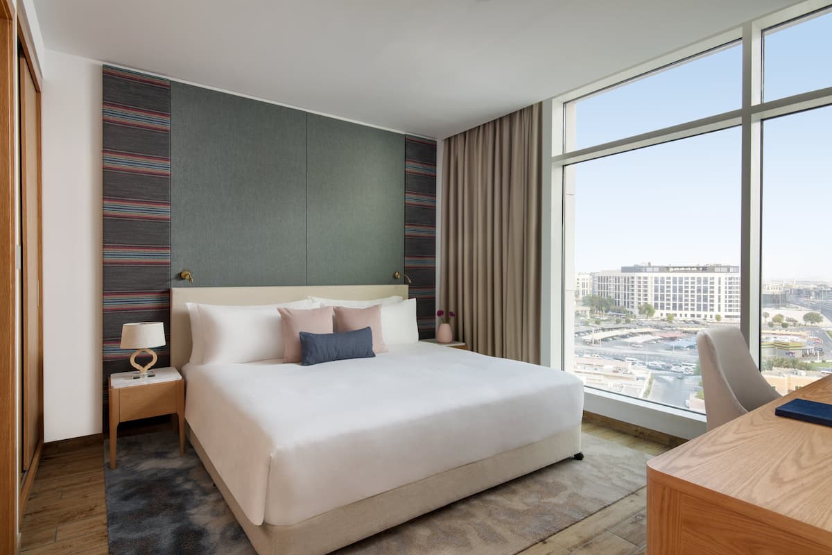 Habitación de hotel con una cama grande, un escritorio y vistas a la ciudad.