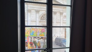 A window with a view of a street scene, including a building with classical architecture and a parked car. - Notre-Dame 3* - OG IMMO (Annecy)
