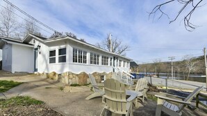 Un edificio blanco con base de piedra, mobiliario exterior con sillas Adirondack y vista a un cuerpo de agua.