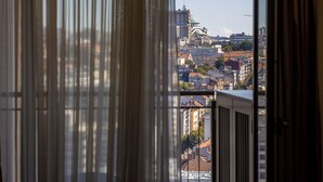A view through a window with vertical blinds, revealing a cityscape with various buildings, including a prominent green-domed structure. - Apartments Royal - Arcadia Building (Belgrade)