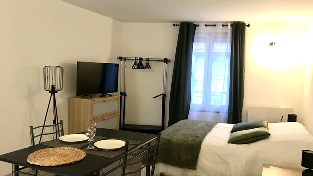 A compact hotel room with a bed, a small desk with a TV, a dining table with chairs, and a standing lamp. - Studio near city center (Verdun)