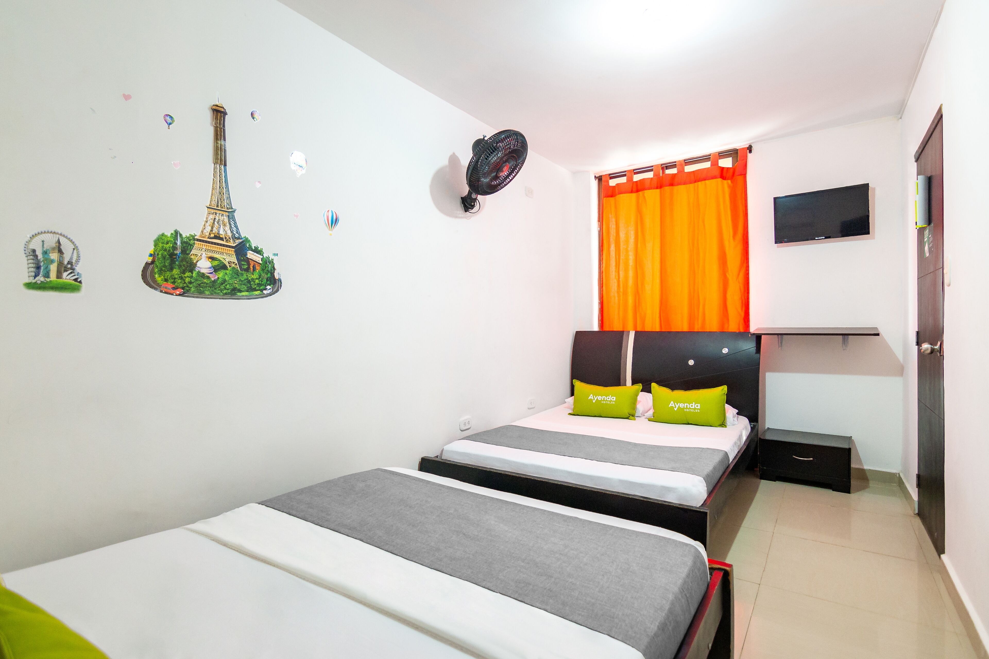 Habitación de hotel con dos camas, un televisor montado en la pared y una ventana con cortinas naranjas.