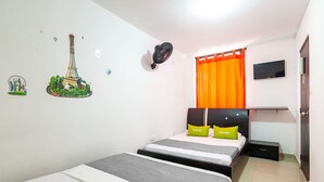 Quarto de hotel com duas camas, uma televisão na parede e janela com cortinas laranja.