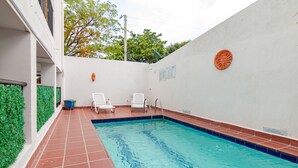 Piscina com deck revestido, duas espreguiçadeiras brancas e uma placa fixada na parede.