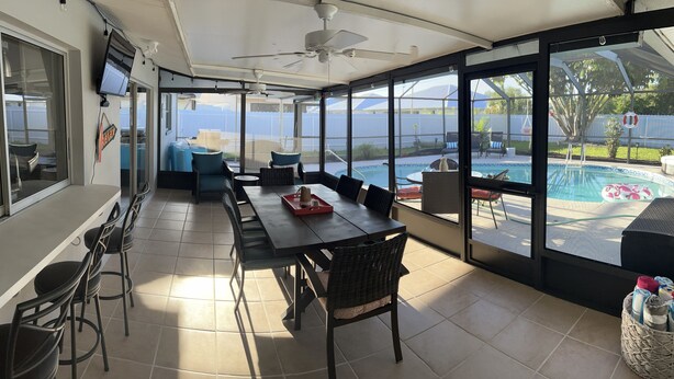 Un patio soleado con vista a la piscina, un comedor con sillas y una mesa, y un ventilador de techo.