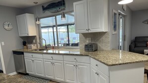 Una cocina con armarios blancos, encimeras de granito, lavavajillas integrado y ventana con vistas a un jardín trasero.