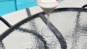 Vista despejada de una piscina con zona de estar techada y una mesa con una bebida.