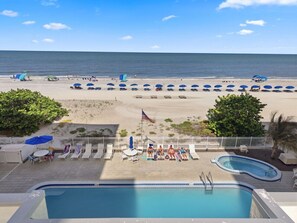 A pool area with a view of the beach, lounge chairs, and umbrellas.
