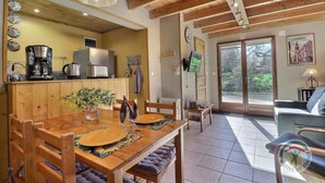 Un rincón comedor acogedor con una mesa de madera, sillas y un florero. Se ve una cocina con electrodomésticos modernos al fondo.