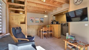 Una habitación acogedora con techo de madera, un sofá, una mesa de comedor con sillas, un televisor y una zona de cocina.