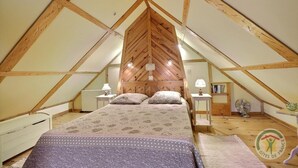 Un dormitorio abuhardinado con techos altos y estructura de madera, una cama con ropa de cama estampada, mesitas de noche con lámparas y un ventilador.