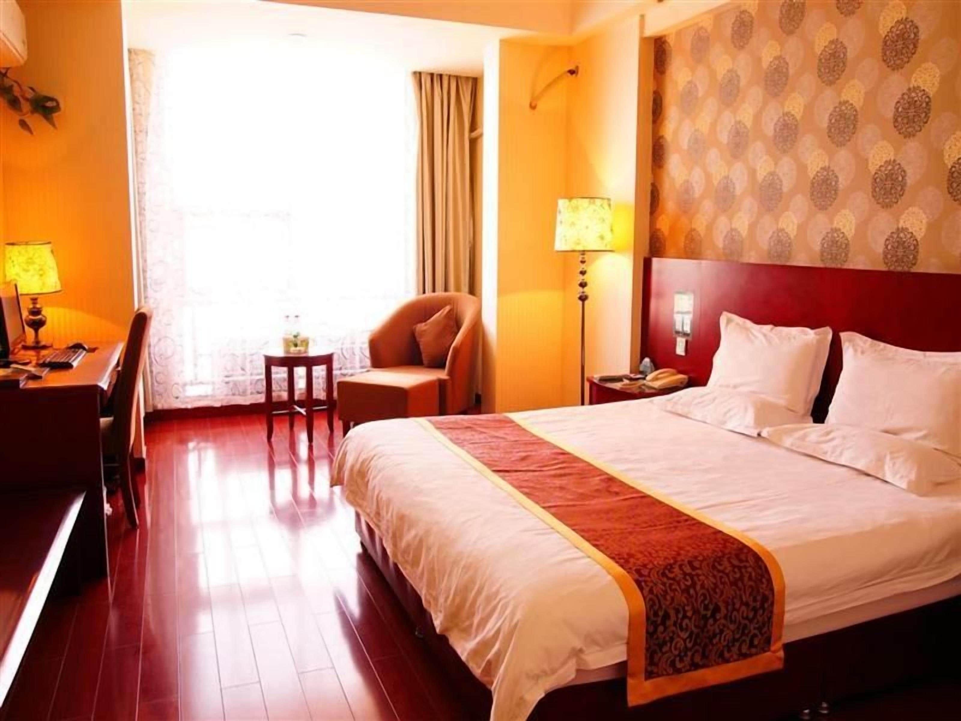 A hotel room with a large bed, a desk with a chair, a small table, and a nightstand with a lamp.
