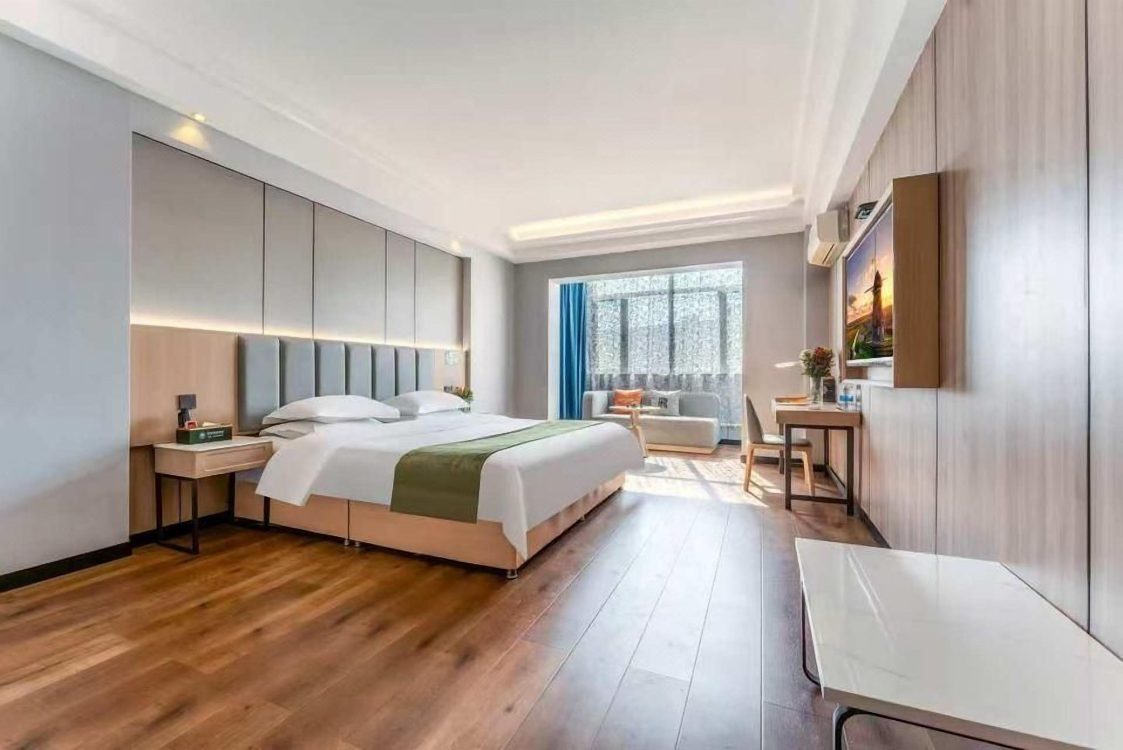 Ein modernes Hotelzimmer mit einem großen Bett, einem Schreibtisch, einem Sessel und einem Fenster mit Vorhängen.