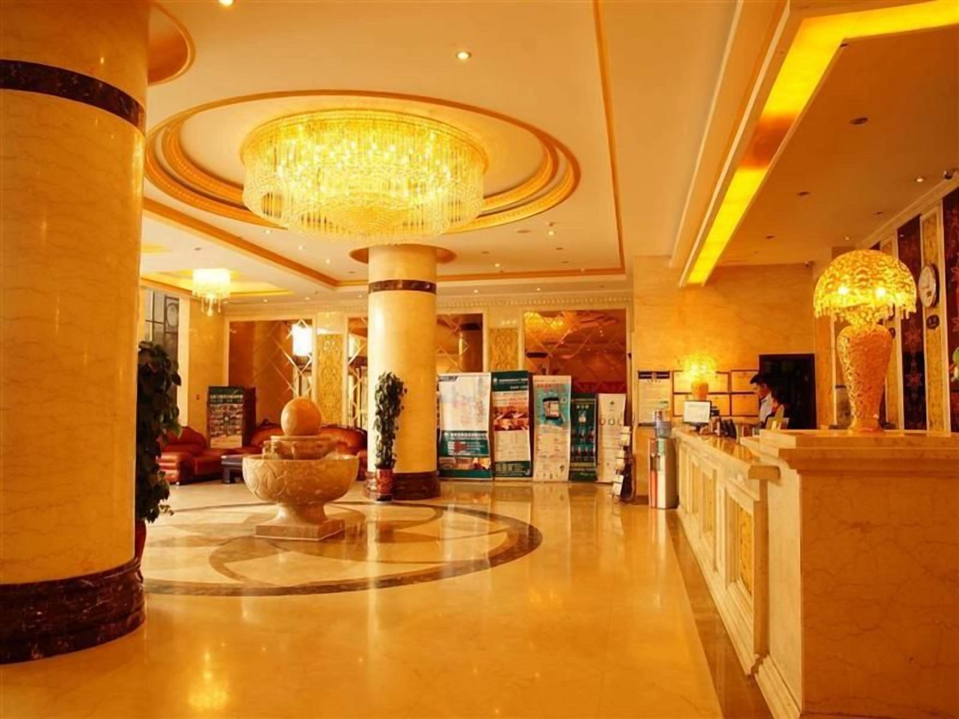 A lobby with a grand chandelier, marble columns, and a reception desk.