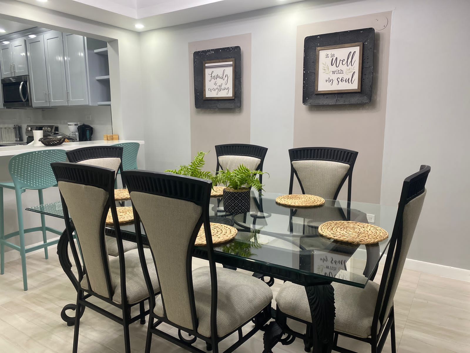 A modern dining area with a glass table, six chairs, and two framed quotes on the wall.