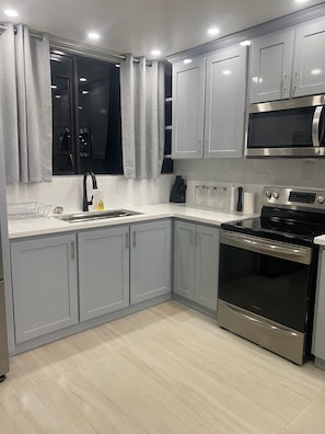 A modern kitchen with grey cabinets, a stainless steel oven, a microwave, and a sink with a black faucet. - Carter's Nest Villa (Kingston)