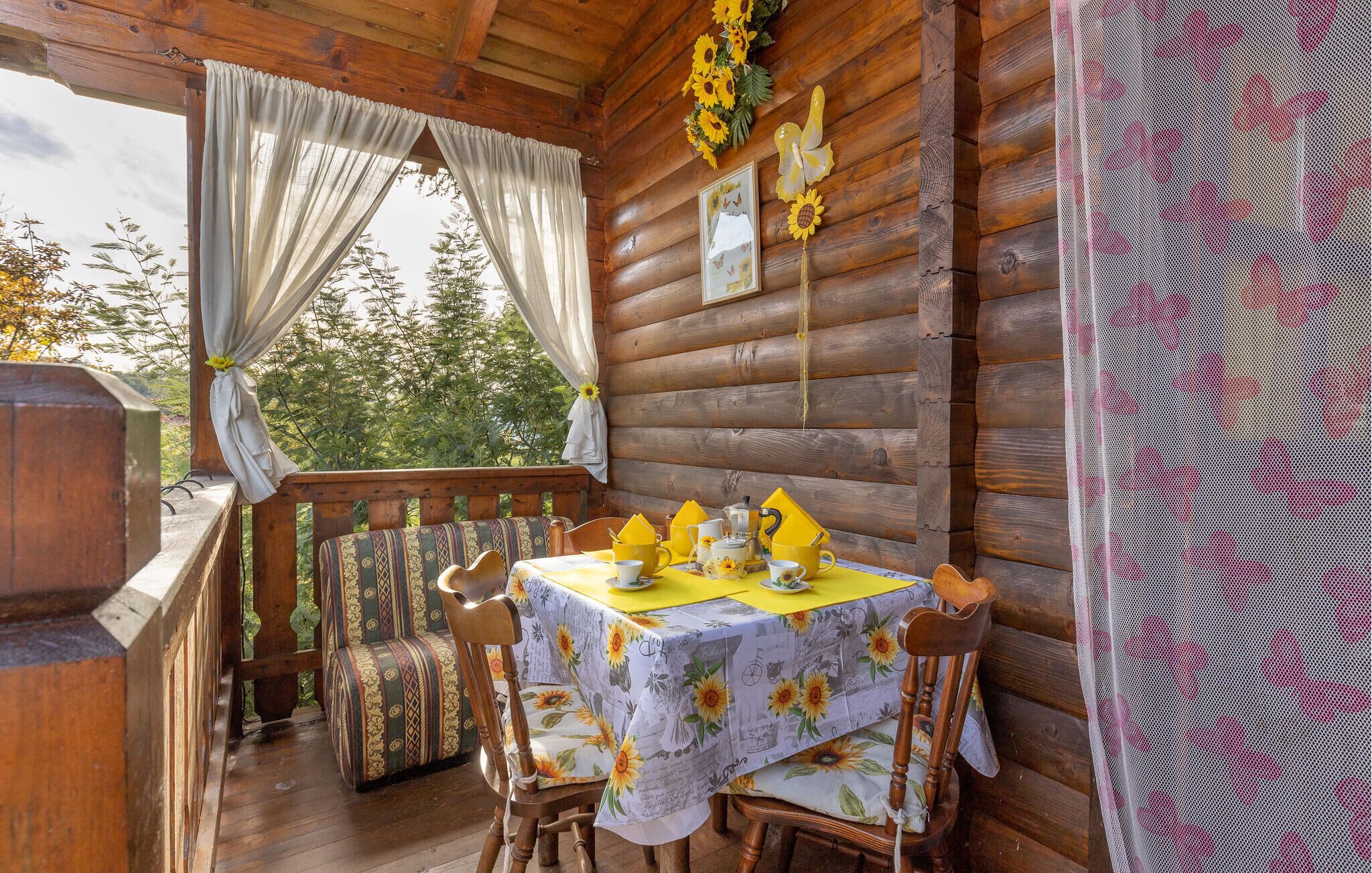 Eine Holzhütte mit Essbereich, ausgestattet mit einem Tisch, gelben Servietten, einer blumigen Tischdecke und Holzsesseln.