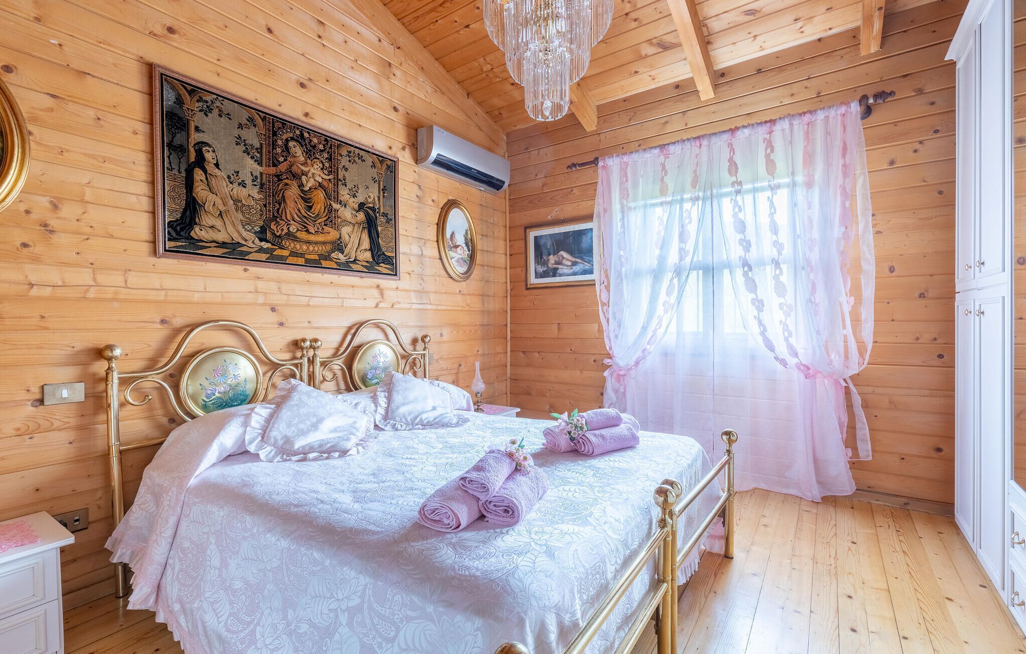 Ein Zimmer mit Holzboden, einem Bett, einer Chandelier und Bildern an den Wänden.