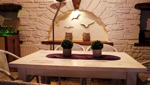 Une table à manger agrémentée de deux plantes en pot, un mur en pierre décoré de motifs d’oiseaux et des chaises en osier.