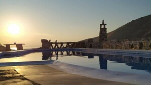 Une piscine en pierre avec un pont en bois et un phare en arrière-plan, au coucher du soleil.