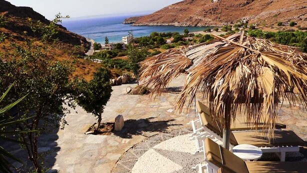 Un sentier de pierres mène à une plage où se trouve une structure recouverte d’un toit de chaume.
