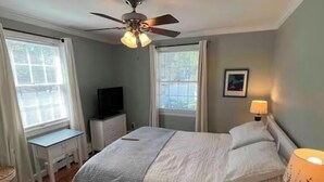 Een slaapkamer met een bed, een plafondventilator, een televisie en een raam.