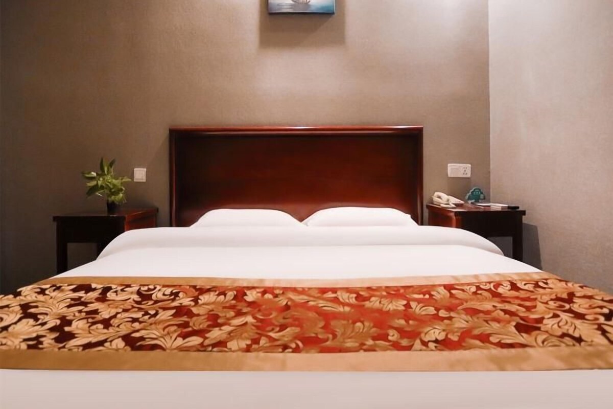 Habitació d'hotel amb un llit gran, un panell de fusta al capçal, una tauleta de nit amb una planta, una taula de nit amb un telèfon i un quadre a la paret.