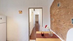 A narrow hallway with a brick wall on one side and a white wall on the other. A table with a candle and a vase of flowers is placed in the hallway. - Oltrarno Suite (Florence)