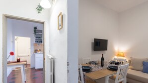 A modern living room with a dining area, white walls, and a flat-screen TV mounted on the wall. - Oltrarno Suite (Florence)